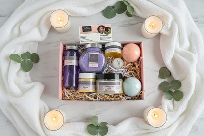 Gift box with bath products and candles on a white marble table. Gift set includes Bath product set with bath bombs, bath salt, body wash, body scrub, face mask, and body butter